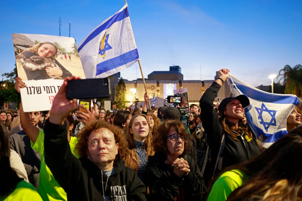 Crowd of people reacting to news of released hostages on television.