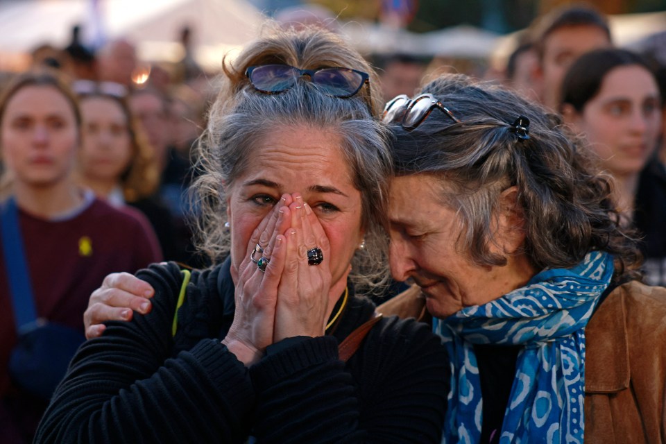 Two women embracing and crying, reacting to news of released hostages.