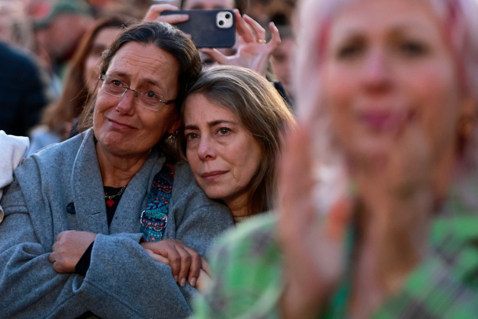 Two women embracing, watching a television broadcast.