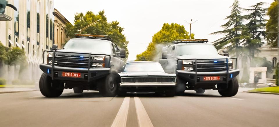 Scene from F9: Fast & Furious 9 showing a car being squeezed by two trucks.
