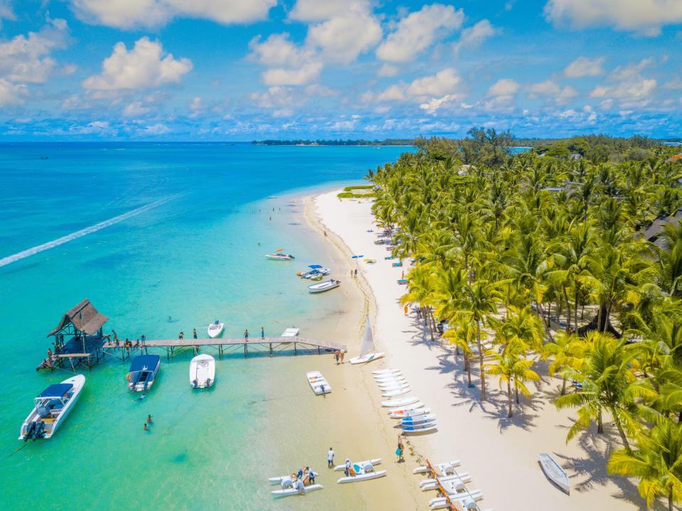 Aerial view of a tropical beach with palm trees, boats, and people.
