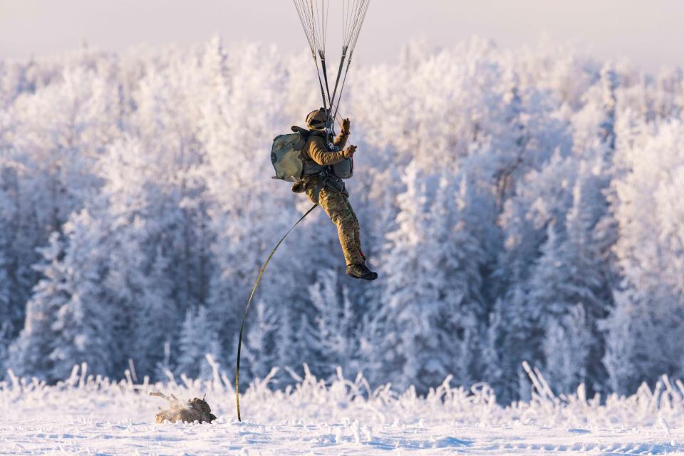 Paratrooper descending over snowy landscape.