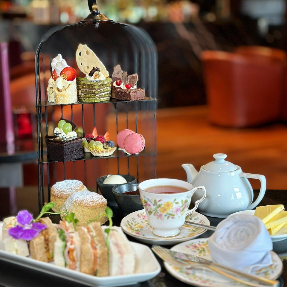 Afternoon tea spread with pastries, sandwiches, scones, tea, and butter.