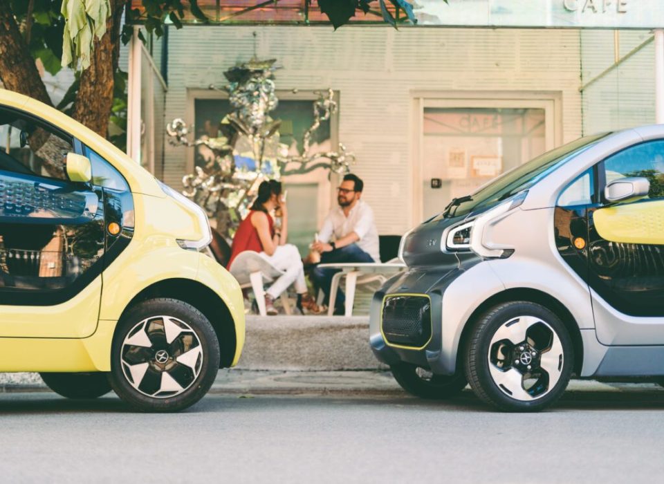 Two electric YOYO PRO cars parked outside a cafe, with a couple sitting at a table in the background.