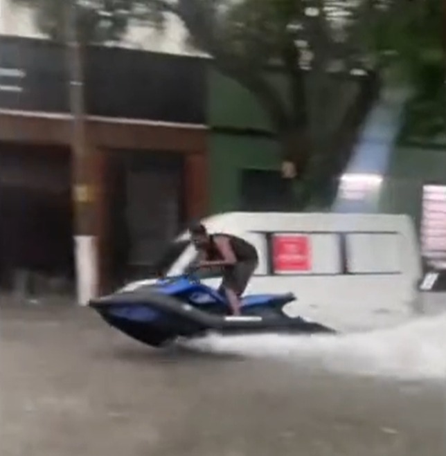 Person riding a jet ski through floodwaters.