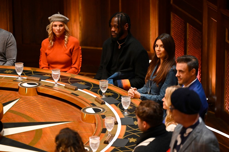 The Traitors contestants seated around a circular table.