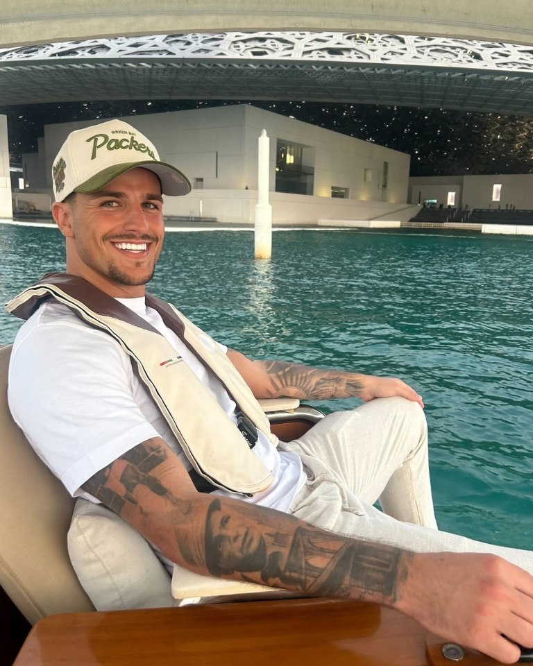 Man wearing a Green Bay Packers hat smiles while sitting on a boat in front of a modern building.