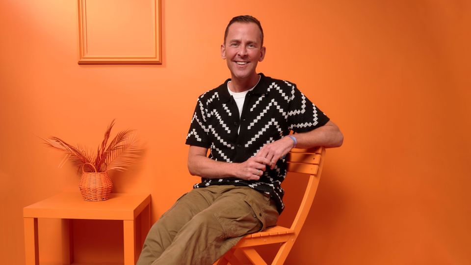 Man sitting in orange chair against orange wall.