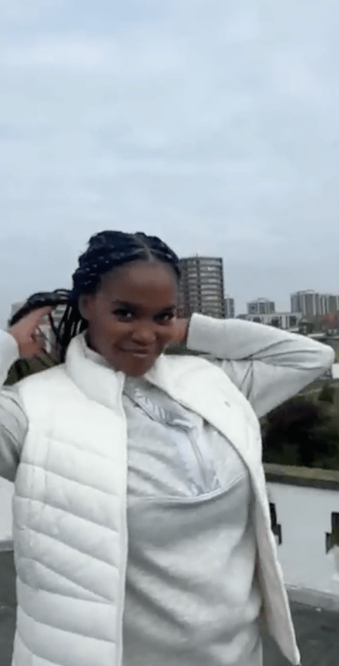 Woman adjusting her braids while wearing a white vest and grey top.
