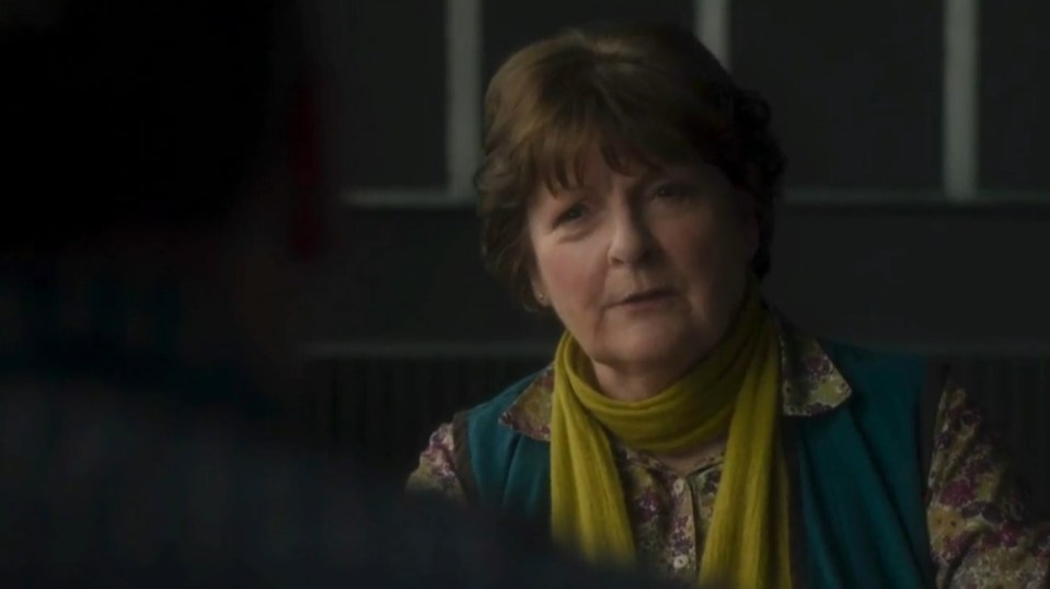 Screenshot of a woman in a teal vest and yellow scarf, speaking to someone off-camera.