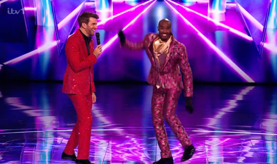 Two men in suits on a stage; one in red, one in pink.