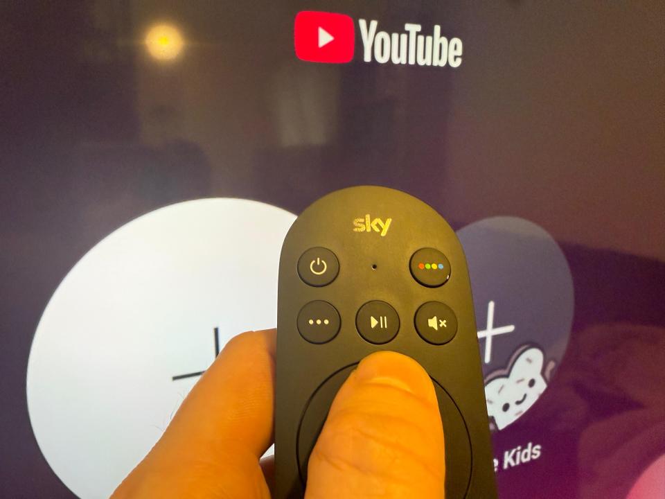 Hand holding Sky remote control in front of a TV screen showing the YouTube logo.