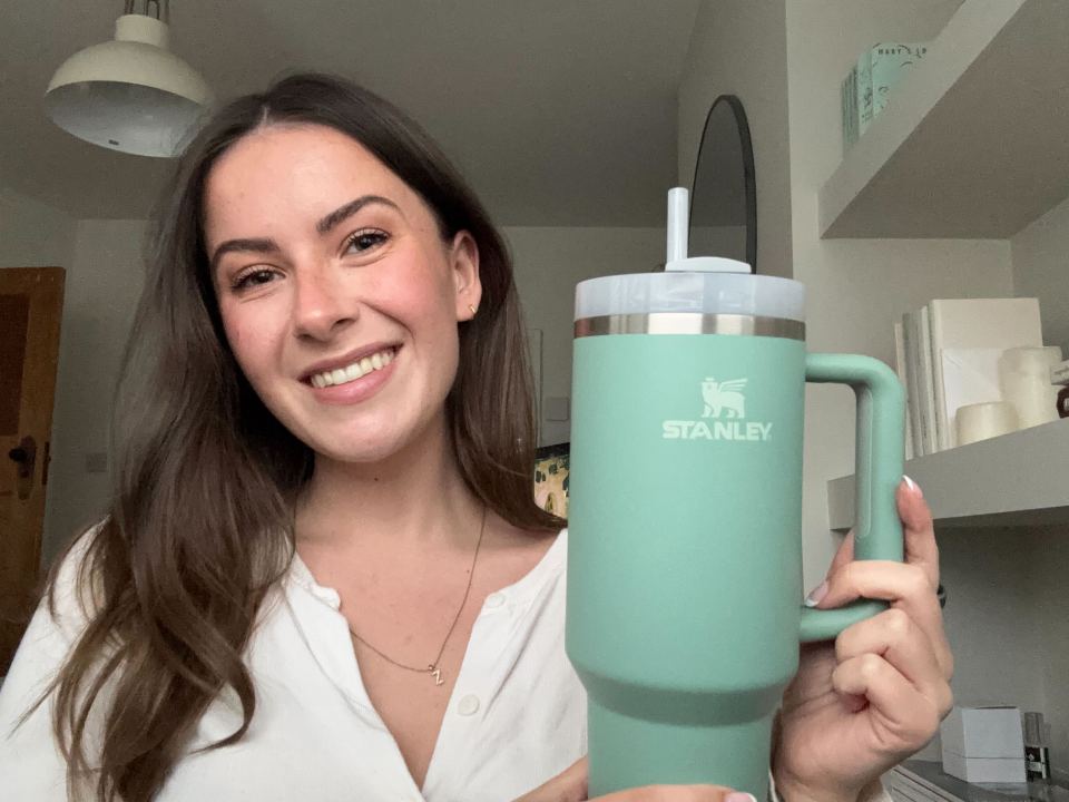 Woman holding a teal Stanley mug with a straw.