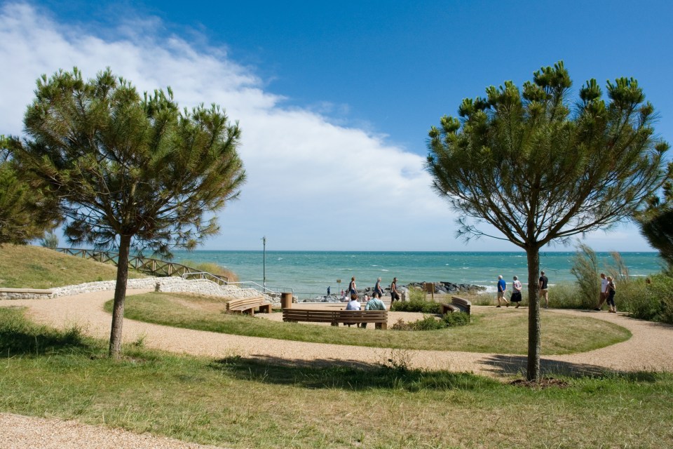 Newly landscaped park area overlooking the sea with benches and people walking.