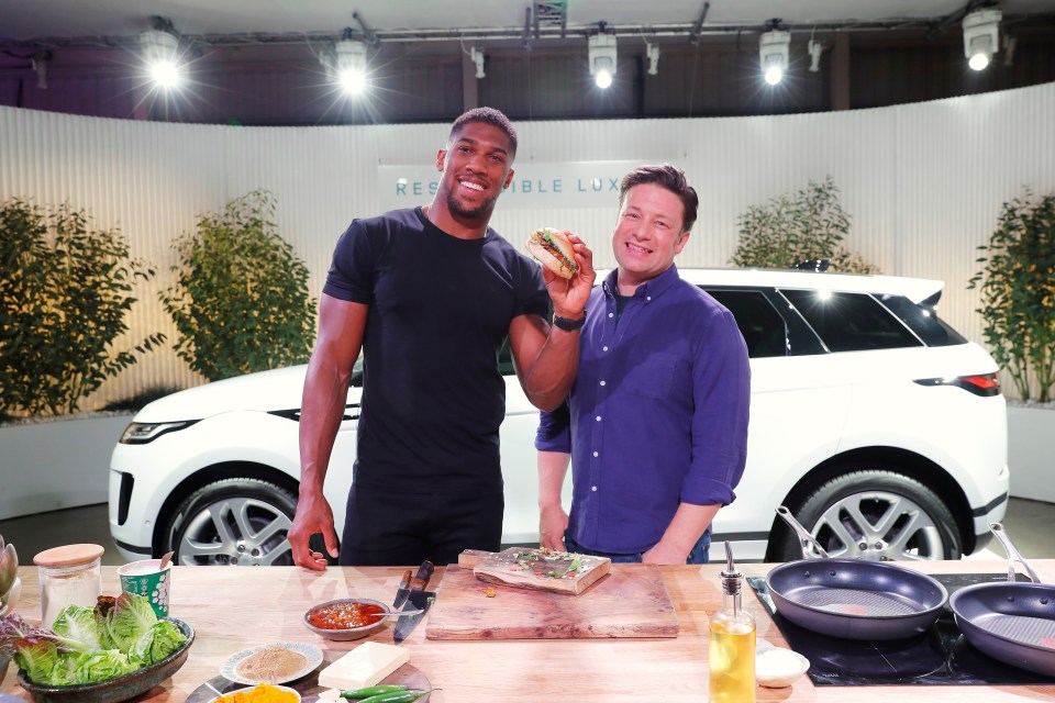 Anthony Joshua and Jamie Oliver holding a burger at a cooking demonstration.