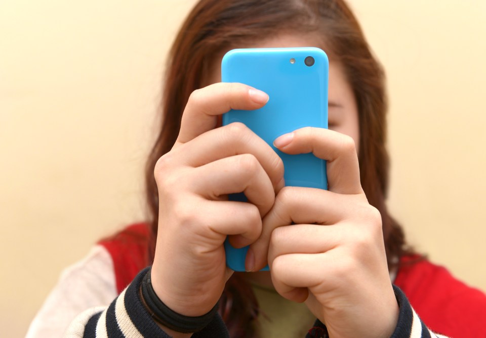 Teenager holding a light blue smartphone in front of her face.