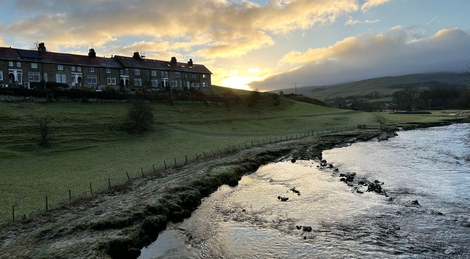 Row of houses on a hillside overlooking a river at sunrise.