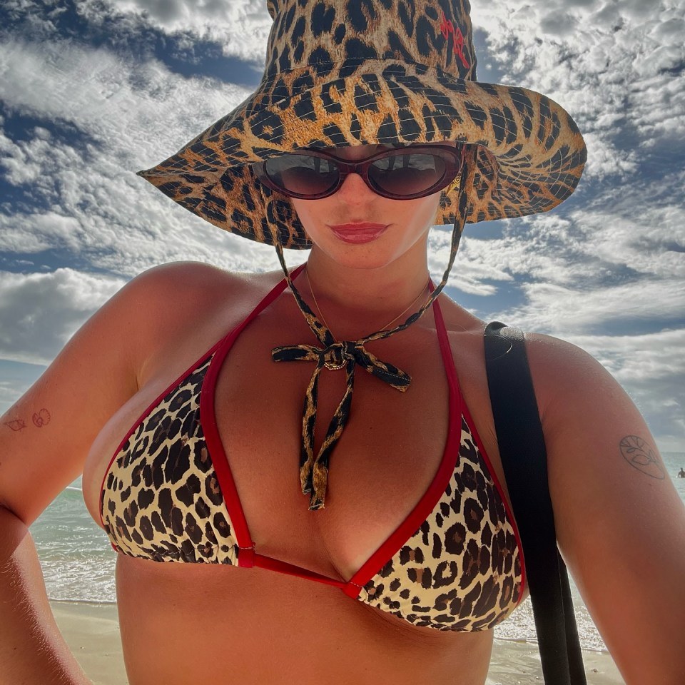 Millie Gibson in a leopard print bikini and hat on a beach.