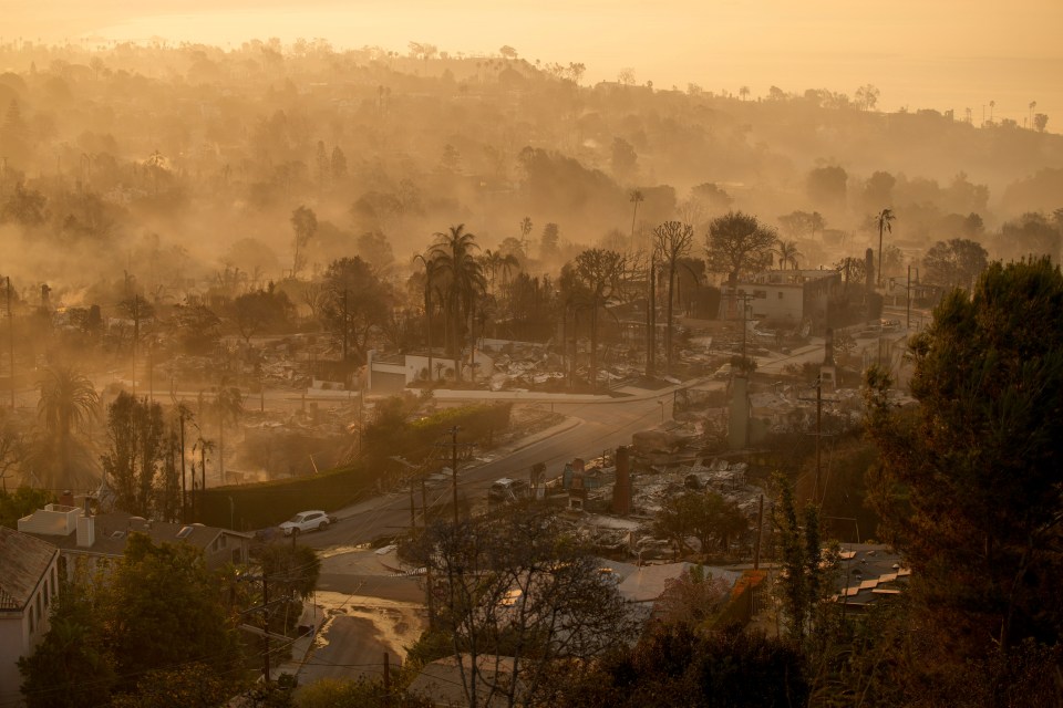 Smoke-filled hillside neighborhood with fire-damaged homes.