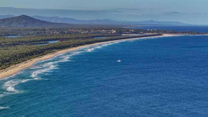 Aerial view of a coastline with sandy beach, ocean waves, and a small boat.
