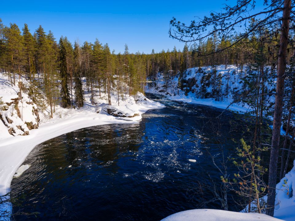 Suspension bridge over a partially frozen river in a snowy forest.