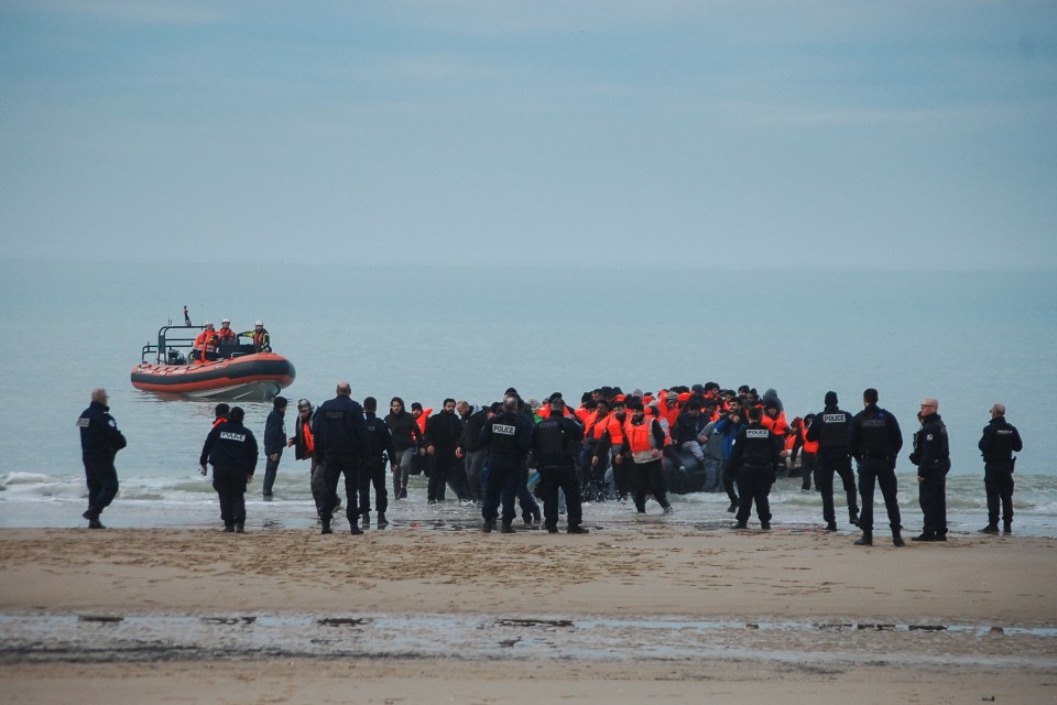 French police officers on a beach with migrants who arrived in an inflatable boat.