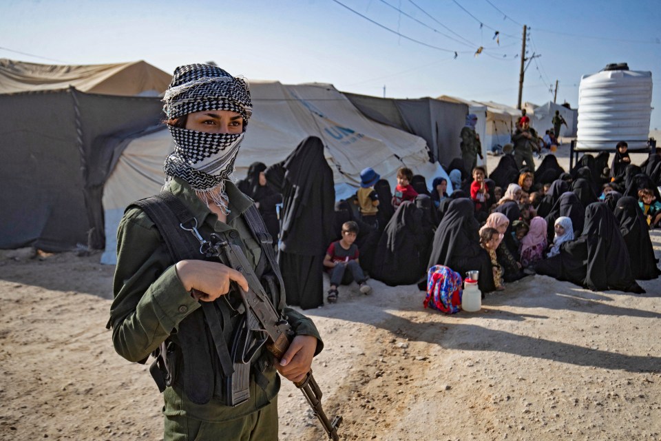 A female Syrian Democratic Forces soldier guards a group of women and children in a displaced persons camp.