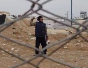 Man seen through chain-link fence, making a gesture.