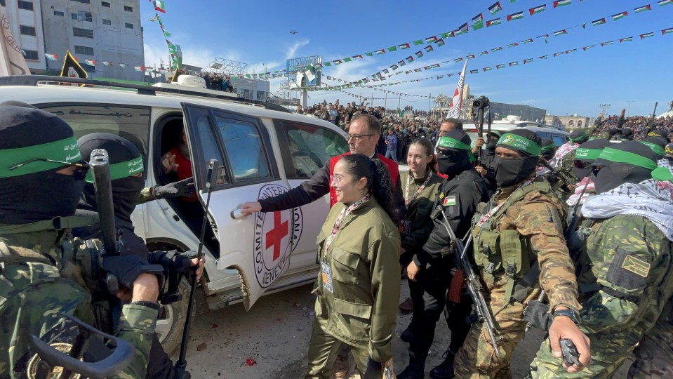 A woman in olive green clothing exits a vehicle with the International Committee of the Red Cross logo, surrounded by armed personnel.