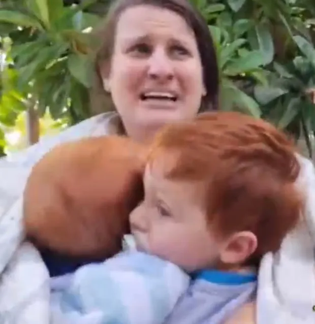 A woman holds two young children close.