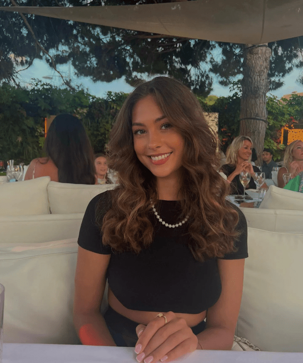 Woman with long brown hair sitting at an outdoor table.