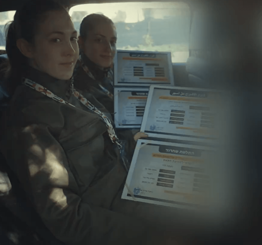 Two women in uniform holding certificates in a car.