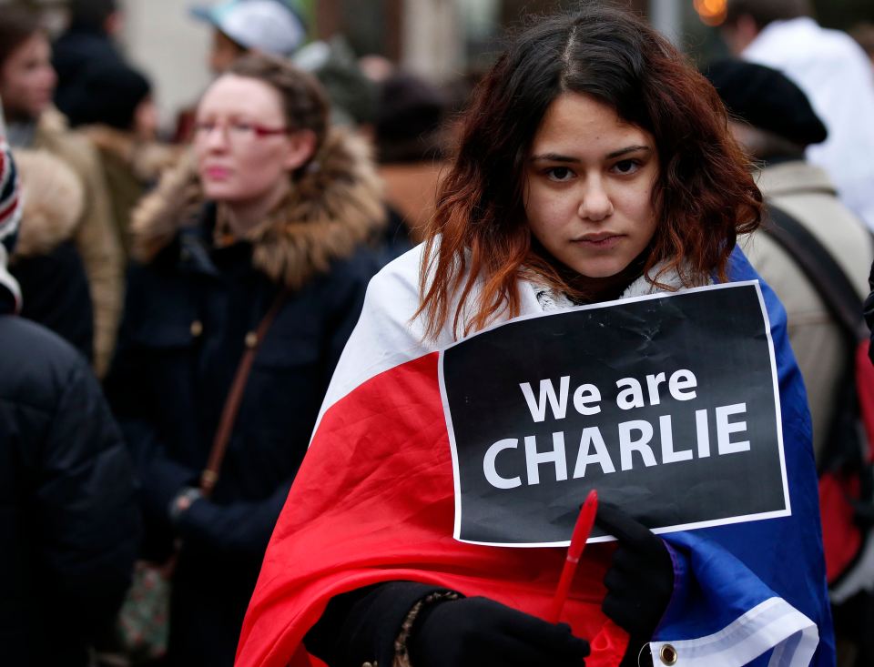 Woman holding a sign that says "We are Charlie" while draped in a French flag.