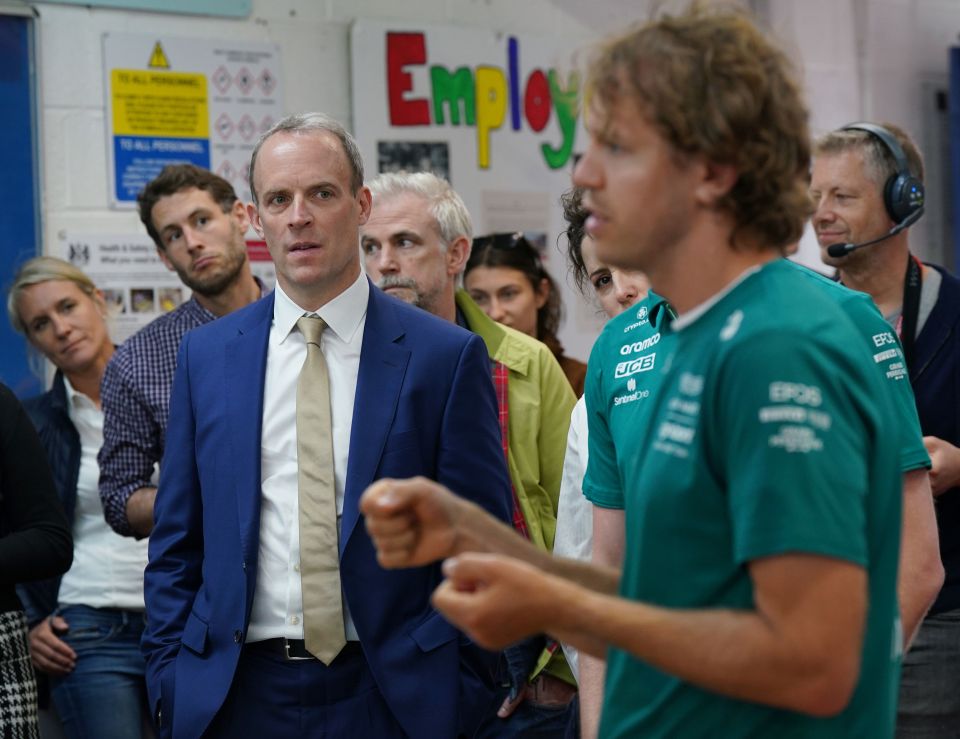 Dominic Raab listening to Sebastian Vettel speak to young offenders at a mechanics workshop launch.