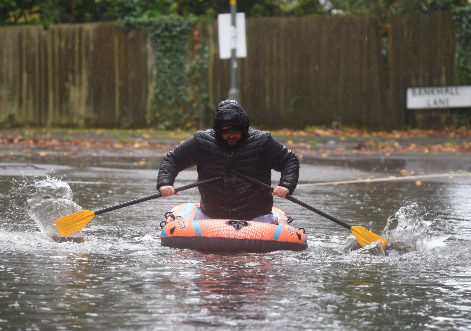 A man paddles an inflatable boat down a rain-flooded street.