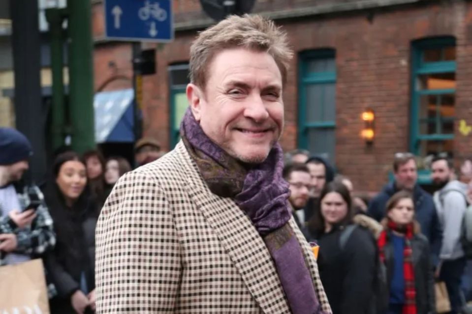 Man in a checked jacket and purple scarf, possibly Simon Le Bon.