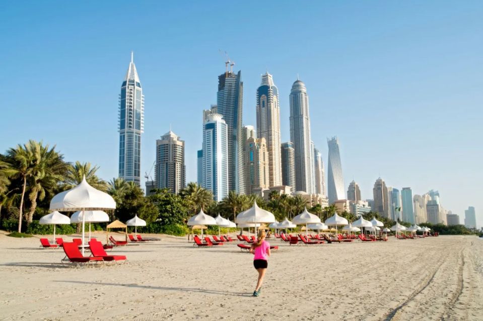 Woman jogging on Dubai beach with skyscrapers in the background.