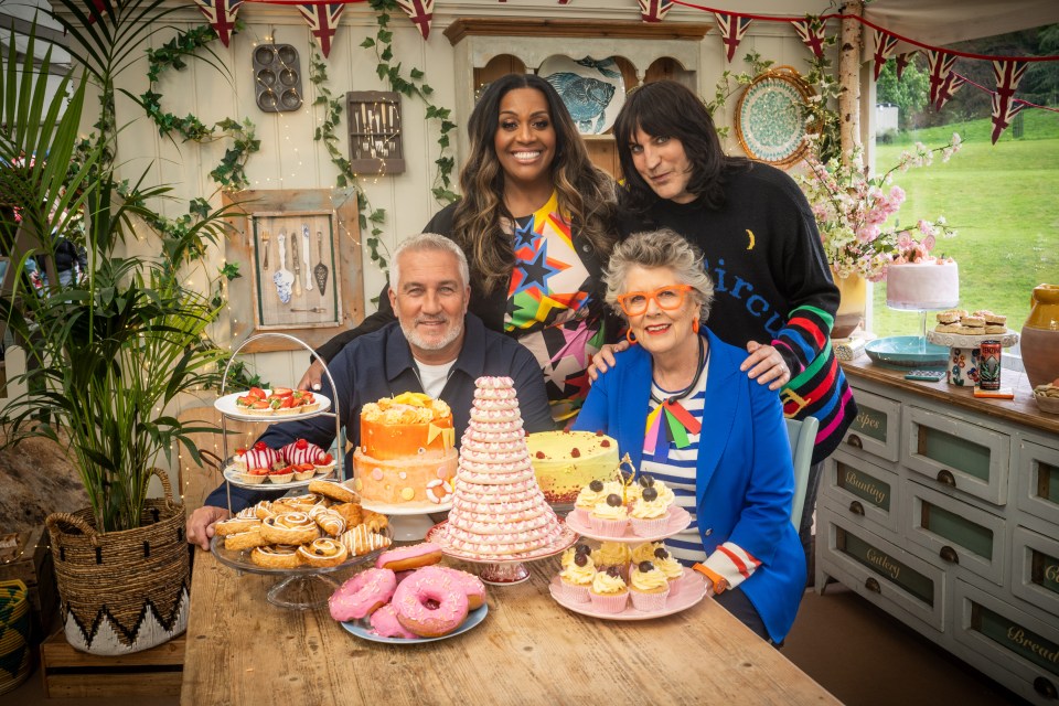The Great British Bake Off judges and hosts, Paul Hollywood, Prue Leith, Noel Fielding, and Alison Hammond, posing together with a table of baked goods.