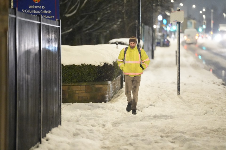 Person walking through heavy snow on a city street at night.