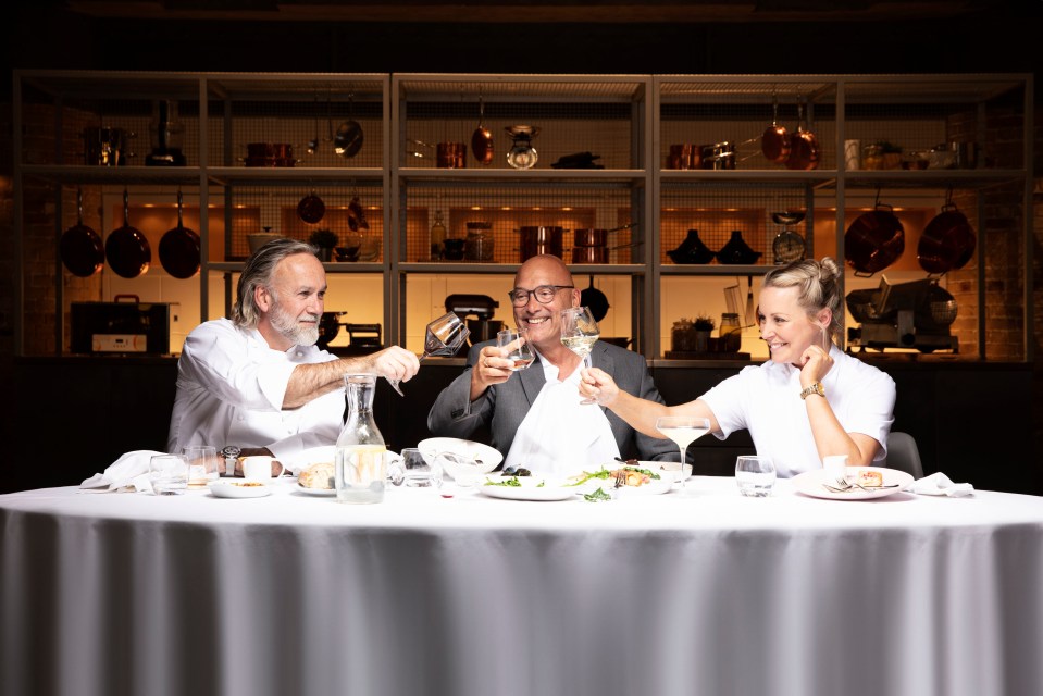 Three MasterChef: The Professionals judges, Marcus Wareing, Gregg Wallace, and Anna Haugh, toasting at a table.