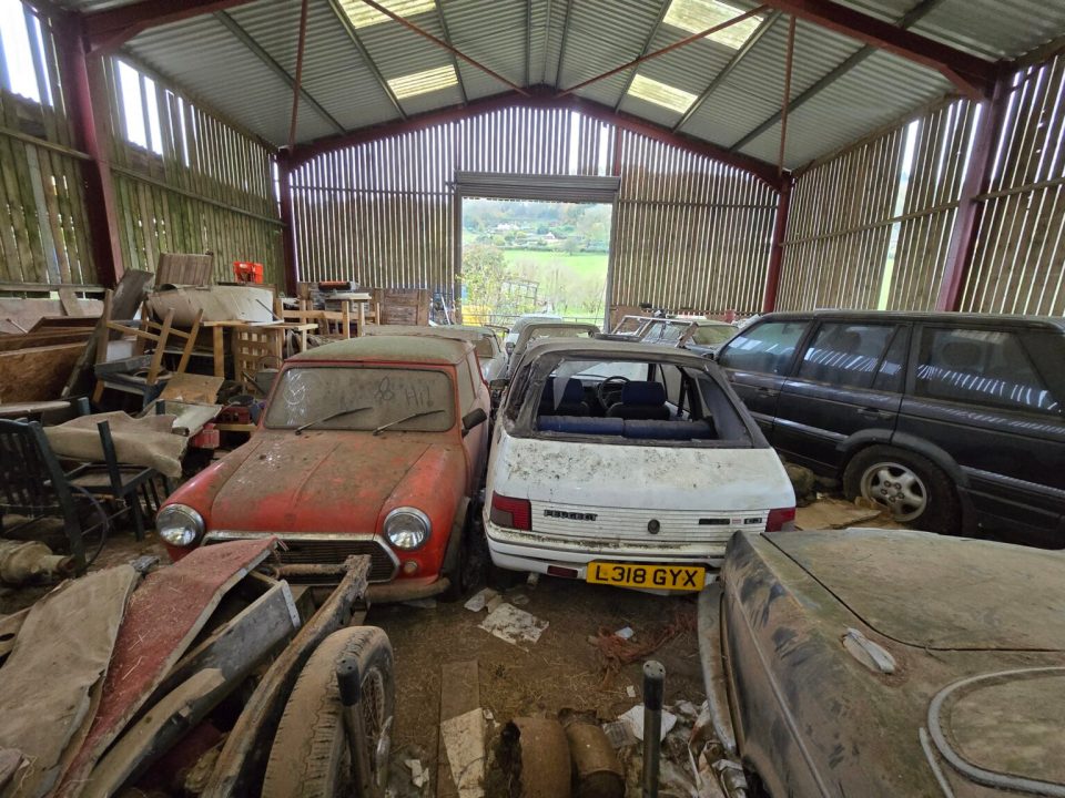 Barn filled with numerous classic cars, some showing significant rust and disrepair.