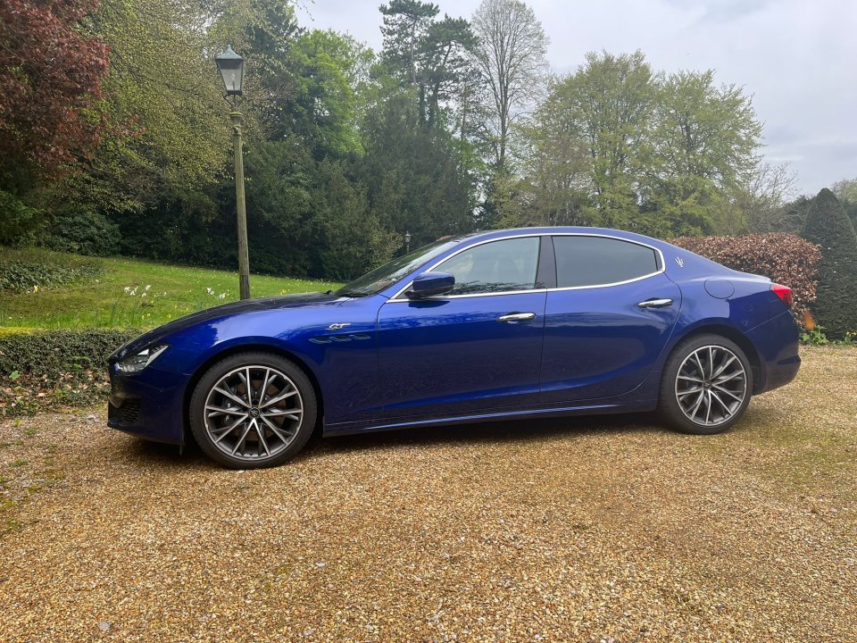 Blue Maserati Ghibli parked in a gravel driveway.