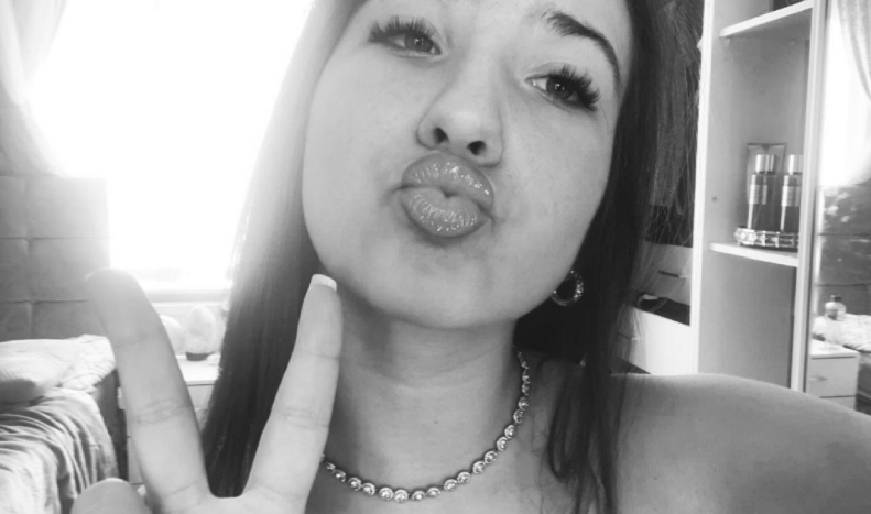 Black and white photo of a girl making a kissy face and peace sign.