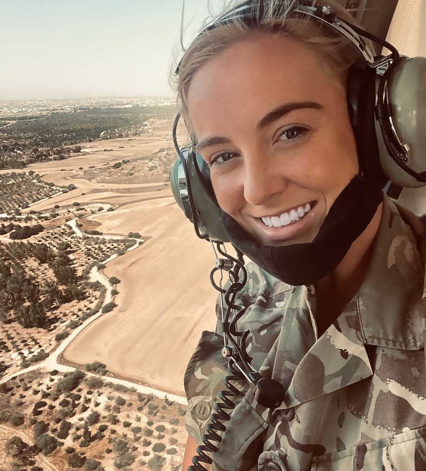 A smiling woman in military uniform in a helicopter, looking at the camera.