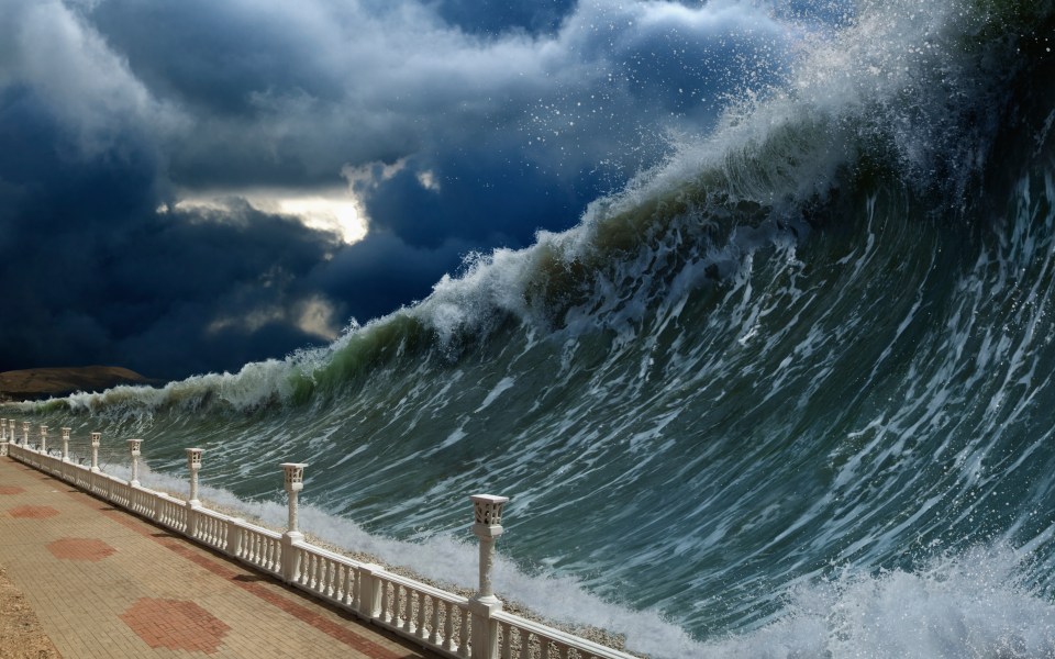 A massive tsunami wave about to crash over a coastal walkway.