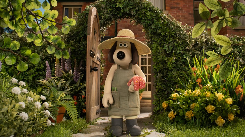 Gromit the dog, wearing gardening attire, stands in a garden.