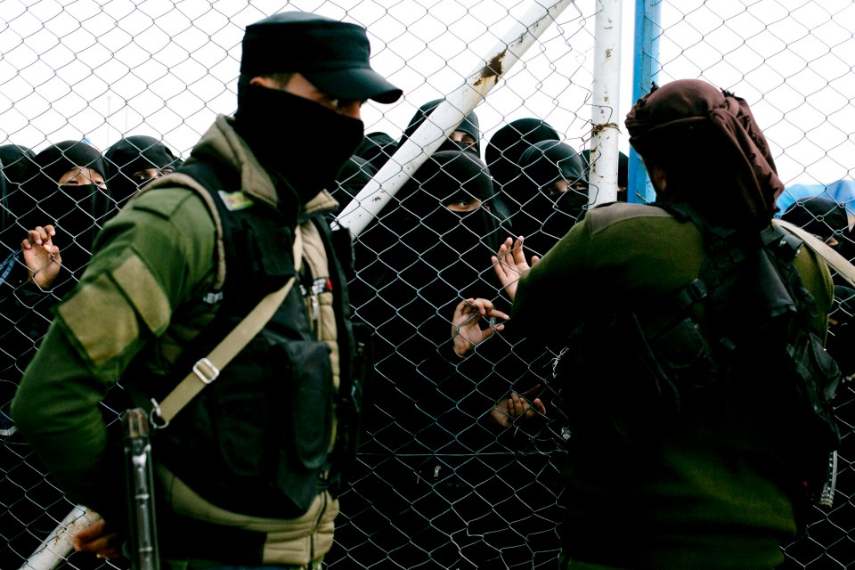 Women in niqabs speak to guards through a chain-link fence.