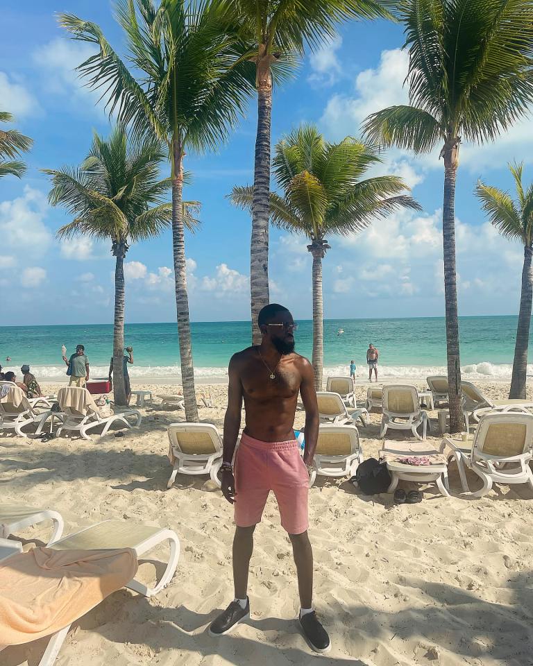 Man in pink shorts standing on a beach with palm trees.