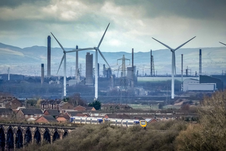 Train passing an industrial area with wind turbines.