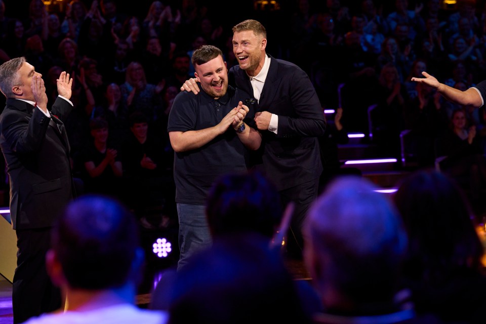Three men on a game show, one with his arm around another.